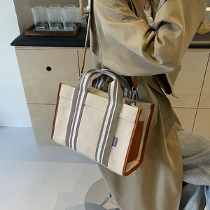 Detail view of canvas tote with brown leather trim and striped strap on model