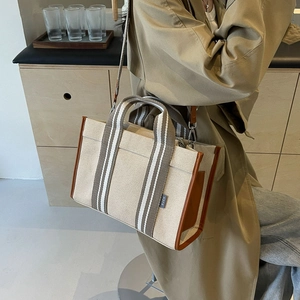 Detail of beige canvas tote bag with brown leather trim and striped strap on model