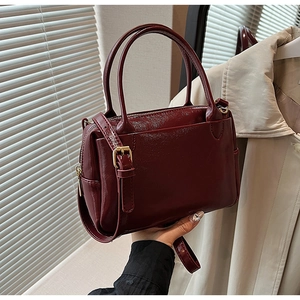Détail du sac à main en cuir verni bordeaux avec finitions dorées et bandoulière