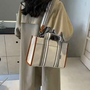 Detail of canvas tote bag with striped straps shown on shoulder for daily commute use