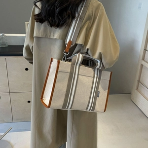 Detail view of beige canvas tote bag with brown leather trim and striped strap on model