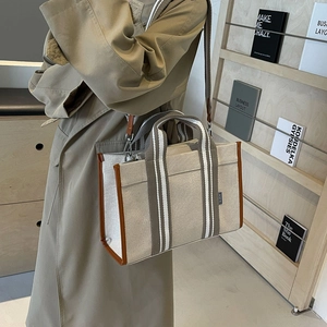 Detail of canvas tote bag with brown leather trim and striped shoulder strap on a model