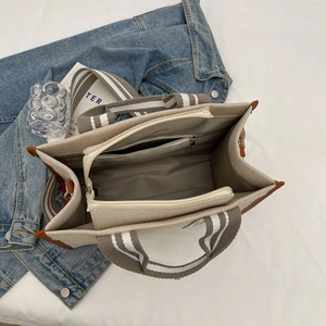 Detail view showing three internal compartments and striped handles of the canvas tote bag
