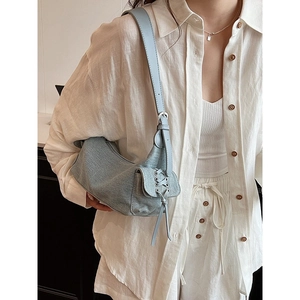 Light blue denim shoulder bag with lace-up details and adjustable strap worn by model