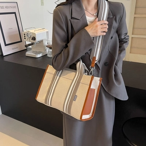 Detail of canvas tote bag with brown leather trim and striped shoulder strap in a cafe setting