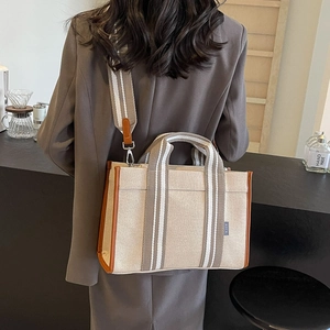 Close-up of large canvas tote bag with brown leather handles and wide striped shoulder strap