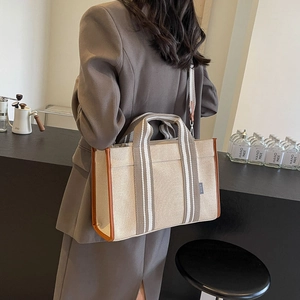 Detail view of canvas tote bag with brown leather trim and striped handle on model