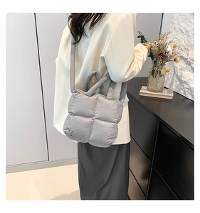 Détail d'un sac matelassé gris avec poignées souples et bandoulière dans un décor