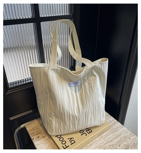 Detail of pleated beige canvas tote bag with brand label on minimalist stone surface