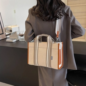 Detail of beige canvas tote with brown leather trim and striped webbing handles