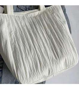 Detailed close-up of white pleated canvas tote bag with woven Kiss Yourself label text
