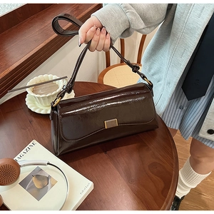 Detail of a dark brown glossy leather shoulder bag with a gold metal clasp on a wooden table