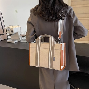 Close-up of beige canvas tote with brown leather trim and SJCH brand label detail