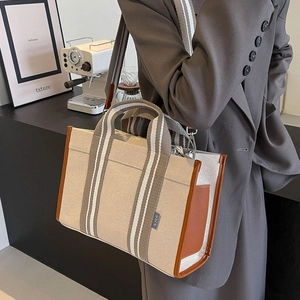 Detail view of canvas tote bag with brown leather trim and striped shoulder strap