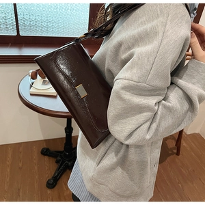 Detail of a dark brown glossy leather underarm bag with metallic buckle on a model