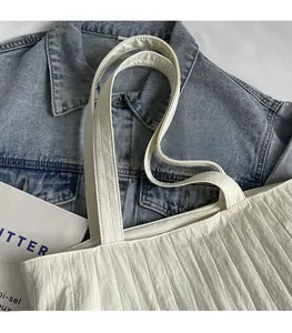 Detailed view of white pleated tote bag featuring woven label on soft canvas texture