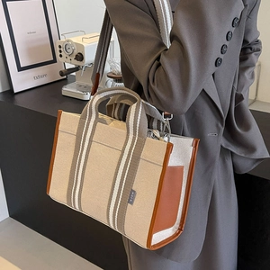 Detail of beige canvas tote bag with brown leather trim and striped shoulder strap