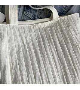 Detail of white pleated tote bag featuring a lavender fabric patch with text embroidery