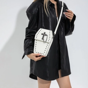 White coffin-shaped gothic crossbody bag with silver cross and stud details on a model