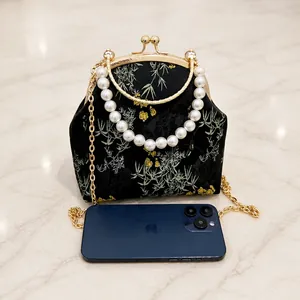 Detalle de bolso bordado chino con asa de perlas y smartphone para comparar el tamaño