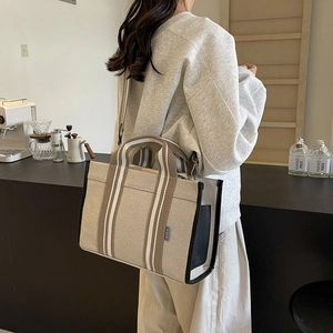 Detail of canvas tote bag with black leather trim and striped strap on model in cafe