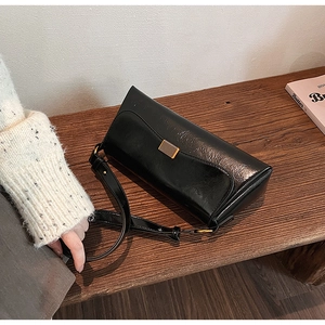 Detail of black glossy leather shoulder bag with elegant gold buckle on a wooden stool