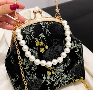 Detalle del bolso de seda bordado negro con asa de perlas y motivo de bambú dorado