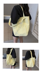 Detail of light yellow corduroy tote bag showing vertical texture and white logo patch