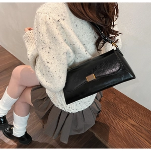 Minimalist black patent leather underarm bag worn by model against a white wall