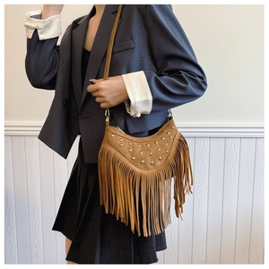 Détail d'un sac bandoulière vintage en daim marron avec rivets dorés et longues franges