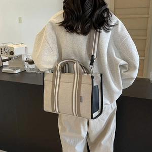 Detailed side view of canvas tote bag with striped straps and black leather trim