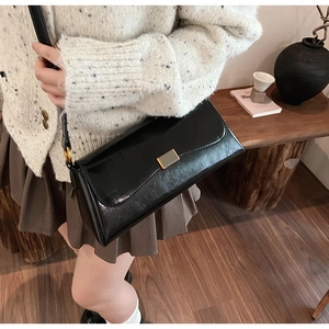 Detail of a black patent leather shoulder bag with vintage gold buckle and glossy finish