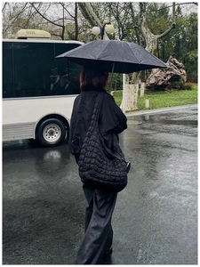 Black quilted puffer bag in hobo style shown in casual outdoor street scene
