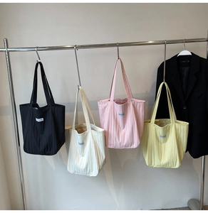 Detail of four pleated tote bags in black, beige, pink, and yellow with shoulder straps
