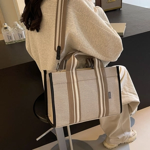 Detail view of large canvas tote bag showing the side leather trim and woven strap texture