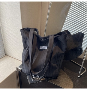 Detailed view of black pleated tote bag fabric texture with minimalist woven label logo