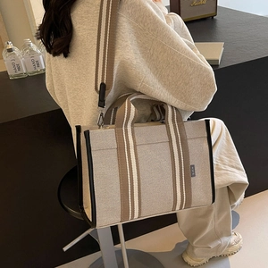 Detailed back view of a large canvas tote bag with striped straps in a minimalist setting
