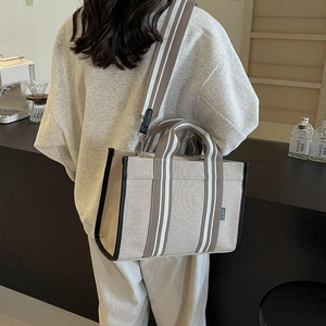 Detail of canvas tote bag showing striped wide strap and logo label in cafe setting