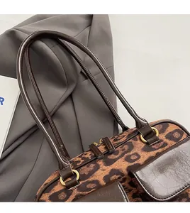 Detail shot of leopard print handbag featuring brown leather trim and golden metal rings