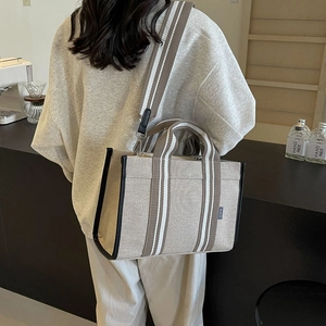 Detailed back view of a large canvas tote bag showing stripe strap on a model