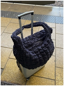 Quilted black puffer bag shown attached to a suitcase handle for easy travel use