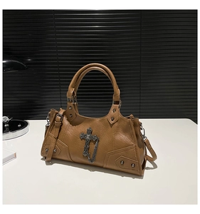 Detailed macro shot of vintage metal cross charm and chains on brown leather punk bag