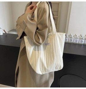 Detail of off-white pleated tote bag with Kiss Yourself logo worn by a model