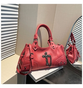 Close-up of red pebbled leather bag with vintage metal cross pendant and rivet details