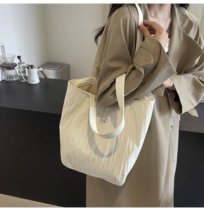Detail view of cream pleated canvas tote bag with wide strap and letter patch