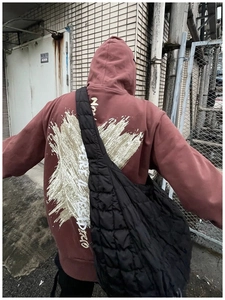 Detailed view of a black quilted puffer crossbody bag paired with a printed hoodie