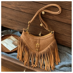 Détail du sac à franges en daim marron avec garniture dorée dans un tiroir vintage en bois