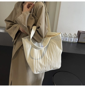 Detail view of cream white pleated tote bag with fine vertical texture and brand tag