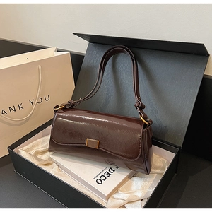 Detail view of dark brown gloss leather baguette bag with gold buckle in black gift box