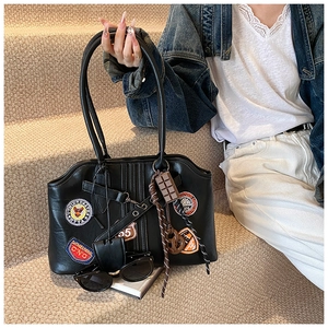 Détail du sac fourre-tout en cuir noir avec badges vintage, broderies et breloques de mode
